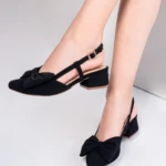 Zapatos de tacón bajo cuadrados para mujer en gamuza negra con cierre de hebilla, estilo destalonado y detalle de lazo frontal decorativo.