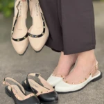 Sandalias destalonadas tipo slingback Tahima con taches dorados; se exhiben en tonos beige, blanco y negro, combinadas con pantalón formal oscuro.