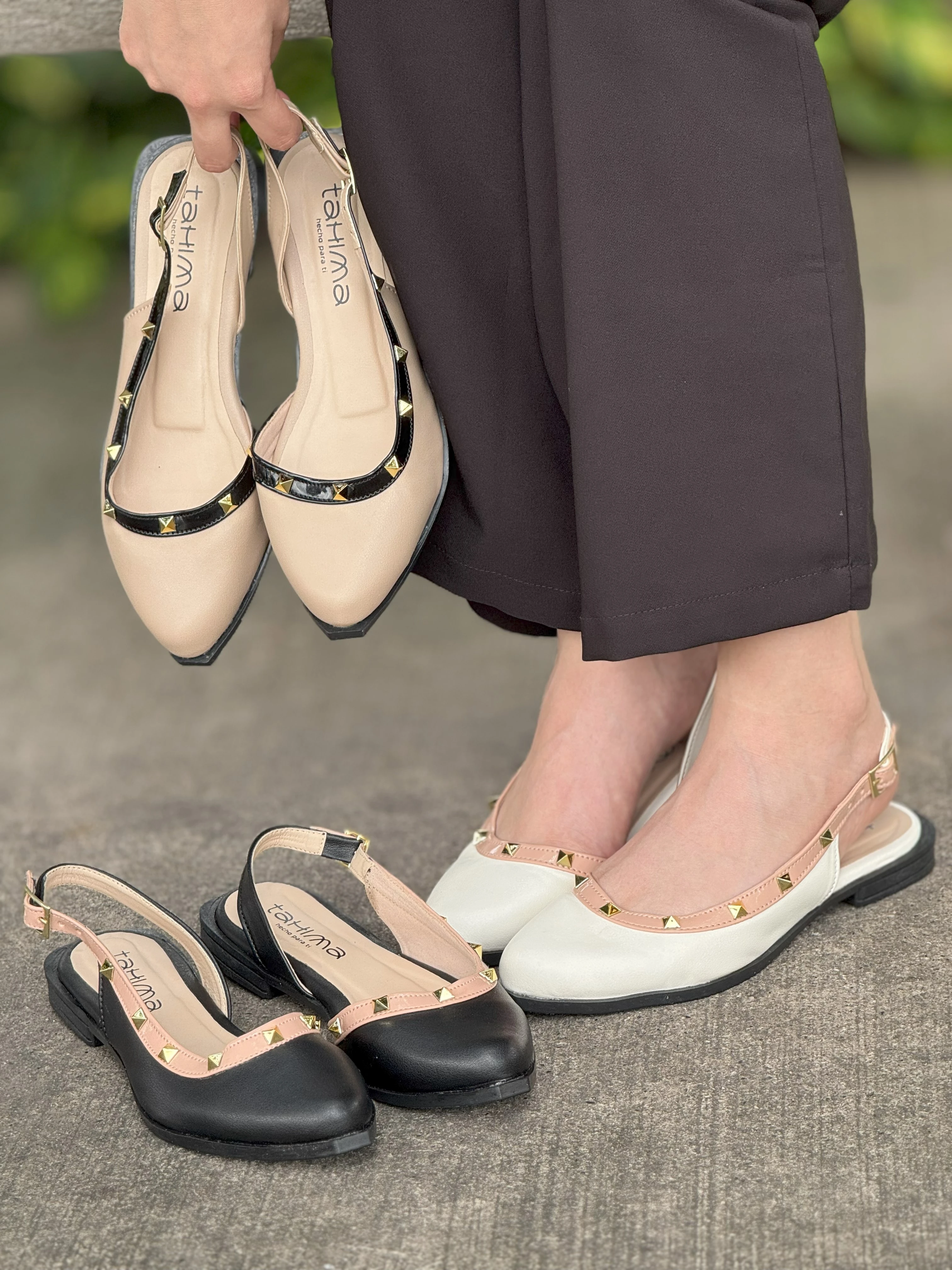Sandalias destalonadas tipo slingback Tahima con taches dorados; se exhiben en tonos beige, blanco y negro, combinadas con pantalón formal oscuro.