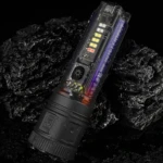 Linterna LED transparente con batería visible, botón de zoom y diseño de alta tecnología, reposa sobre rocas negras húmedas.