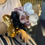 Muñeca de mujer con cuatro scrunchies de satén en colores blanco, rosa, negro y dorado, exhibidos para resaltar su textura brillante y acabado elegante.