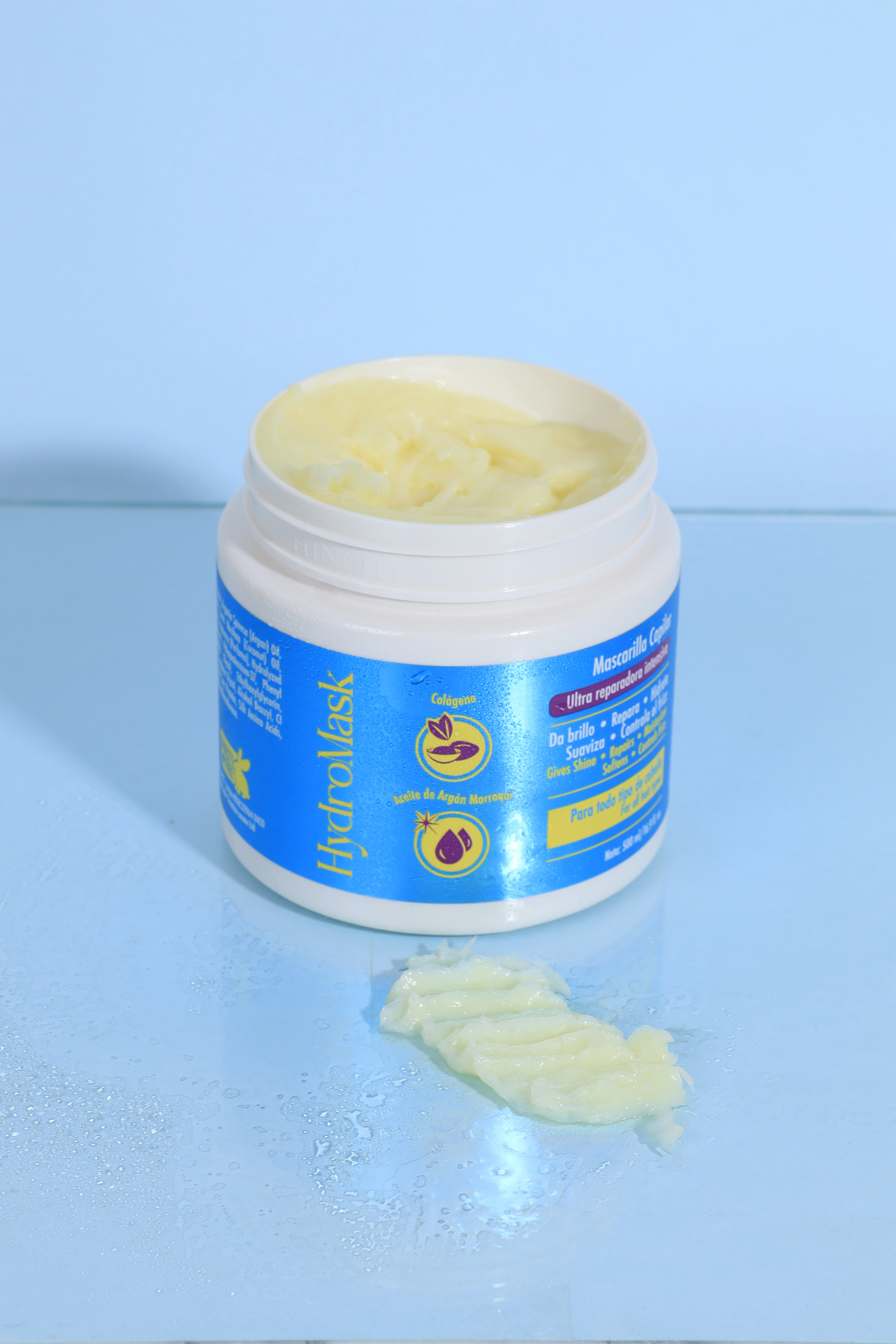 Mascarilla capilar Hydromask 500ml, envase blanco, crema amarilla, sobre superficie mojada.