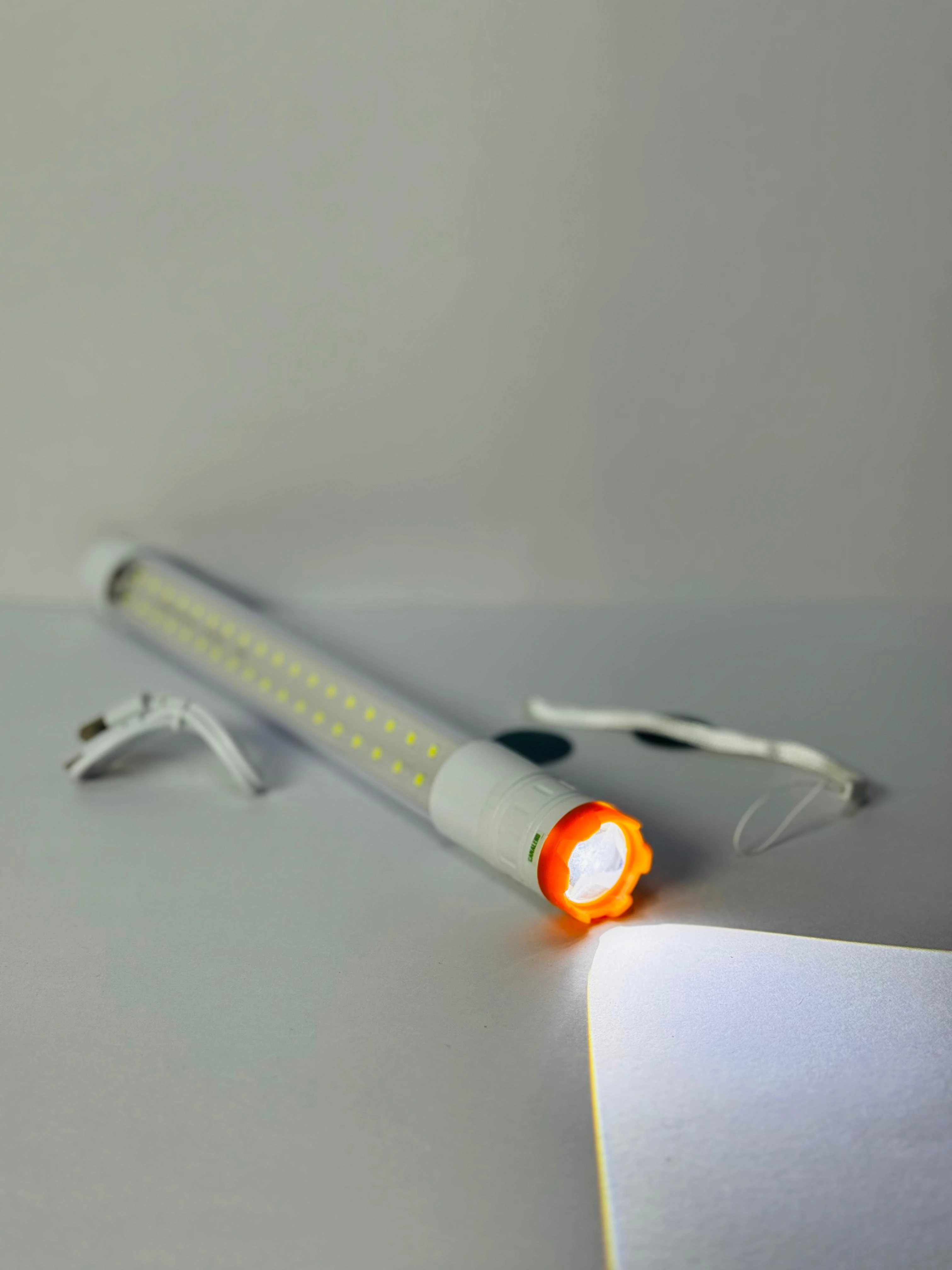 Linterna LED blanca de 27cm con luz frontal naranja, cable USB y cordón.