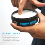 Cera para peinar Forming Cream L3 de textura cremosa blanca en tarro negro, sostenida por una mano mientras un dedo toma una pequeña porción del producto.