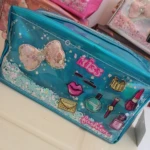Cosmetiquera azul transparente con figuras de moda, lentejuelas y moño, con fondo de brillos y confeti.