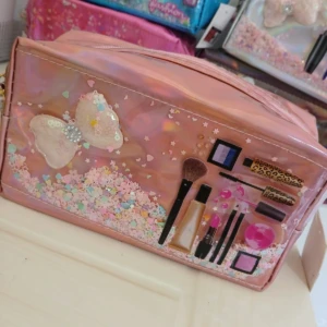 Cosmetiquera rosa holográfica con aplicación de moño, confeti líquido y diseños de maquillaje.
