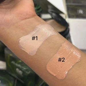 Prueba de dos tonos de base cushion sobre la piel del antebrazo: el tono 1 presenta un matiz claro rosado y el tono 2 un matiz medio cálido y bronceado.