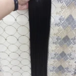 Extensiones de cabello liso color negro de 60 cm, presentadas en una cortina con cinco ganchos de sujeción, sostenidas verticalmente por una mano.