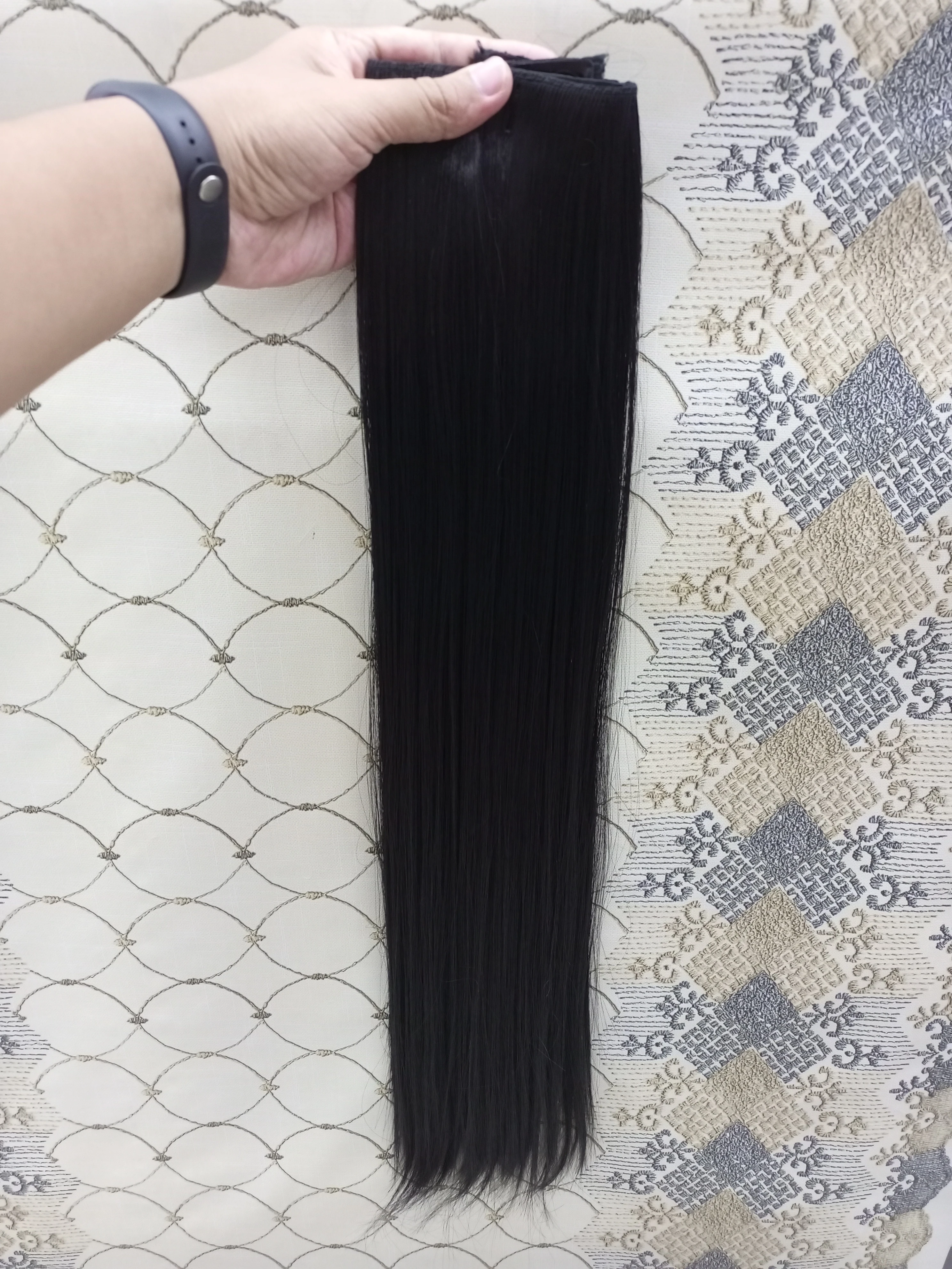 Extensiones de cabello liso color negro de 60 cm, presentadas en una cortina con cinco ganchos de sujeción, sostenidas verticalmente por una mano.