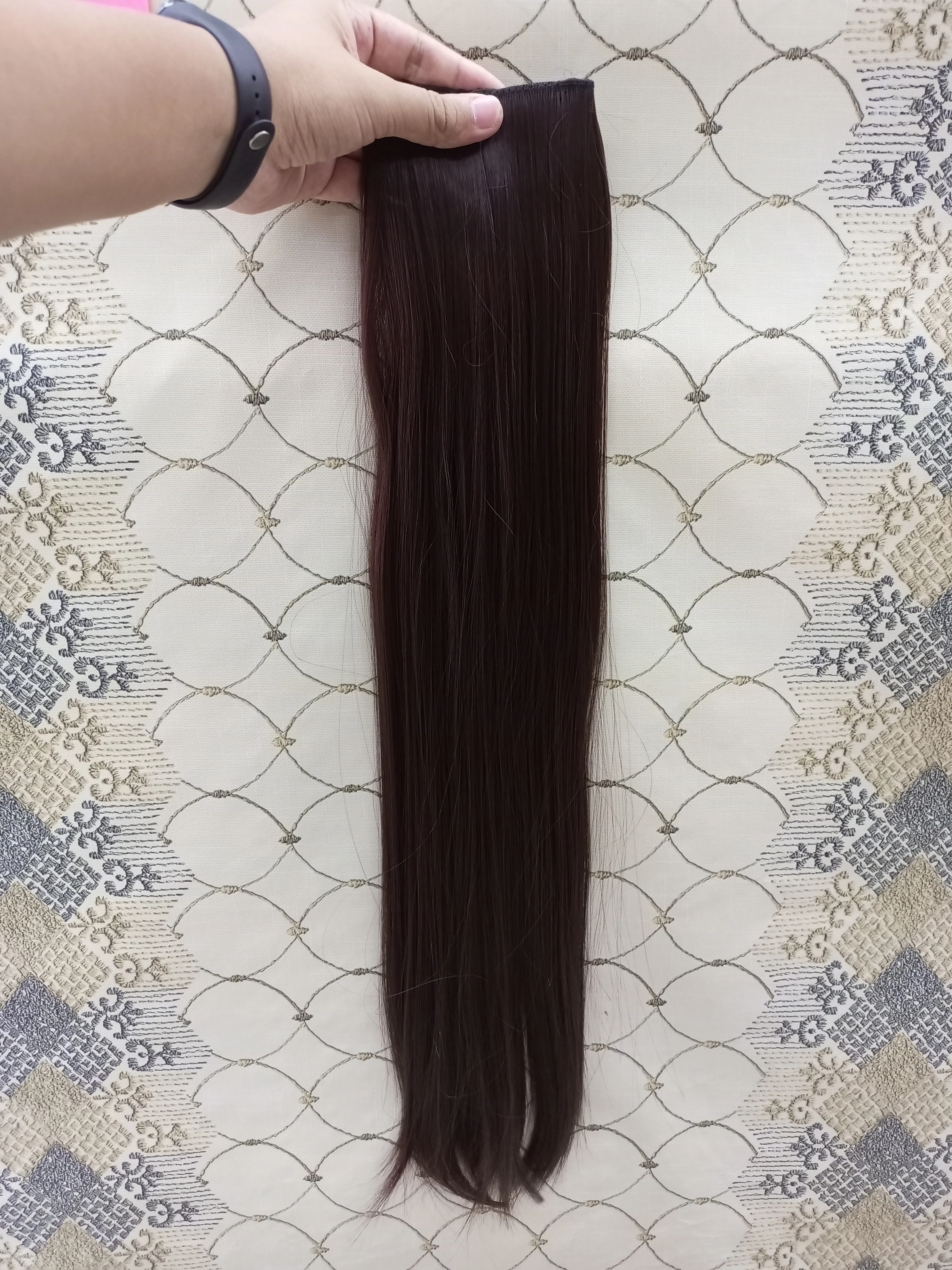 Extensiones de cabello liso color castaño oscuro de 60 cm, sujetas por una banda superior con clips, mostradas sobre un fondo decorativo claro.