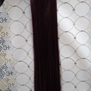 Extensiones de cabello liso color borgoña de 60 cm, sujetas por una banda con ganchos, presentadas sobre un fondo de tela con estampado de líneas blancas.