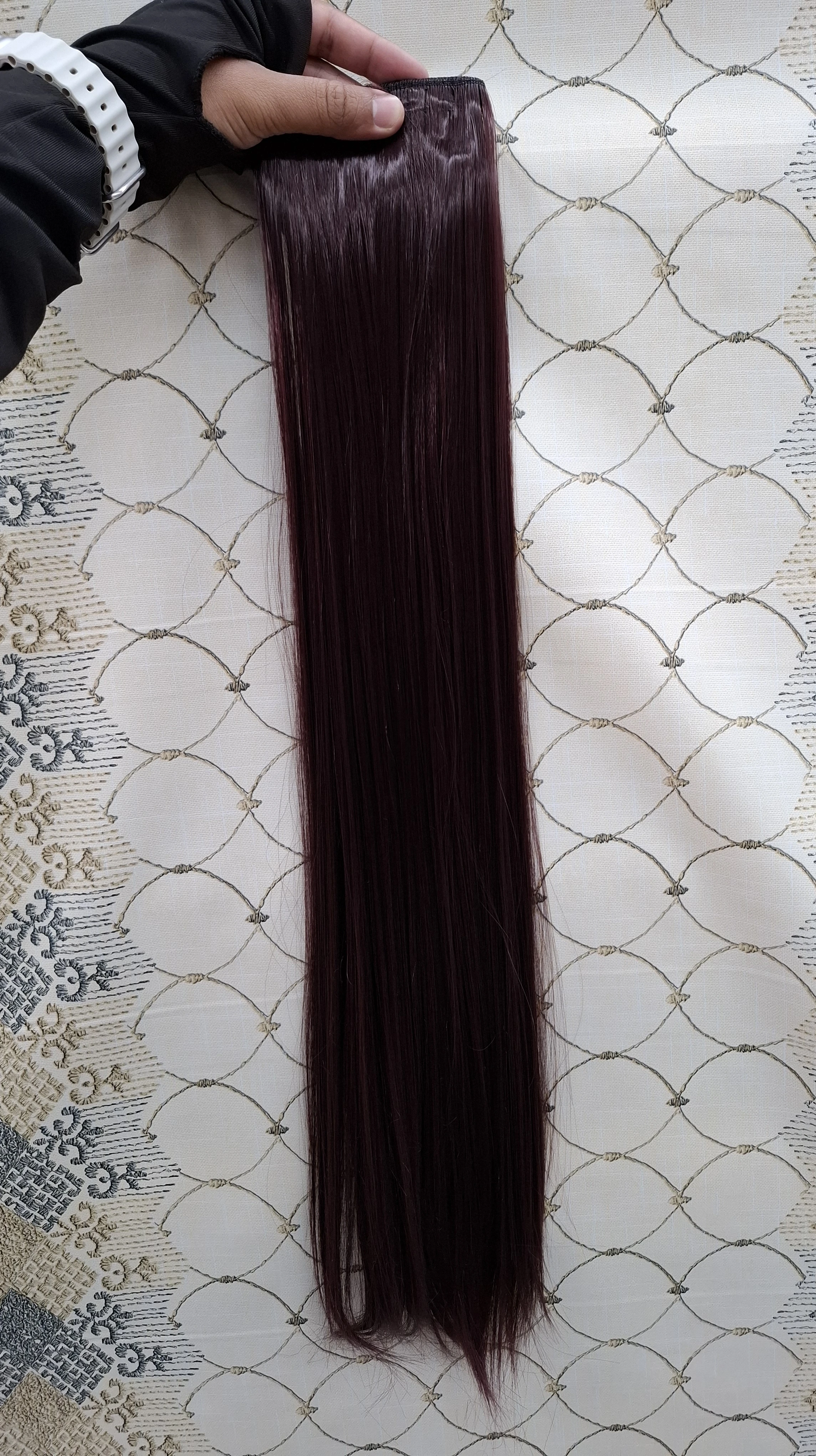 Extensiones de cabello liso color borgoña de 60 cm, sujetas por una banda con ganchos, presentadas sobre un fondo de tela con estampado de líneas blancas.