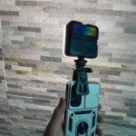 Luz LED RGB para celular con clip, montada en funda protectora plateada con soporte para anillo.