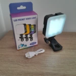 Luz LED portátil AY-83 con clip para celular, en caja y cable USB, sobre superficie de madera.