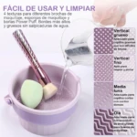 Recipiente morado con texturas para limpiar brochas de maquillaje, agua vertiéndose, esponja verde y brocha.