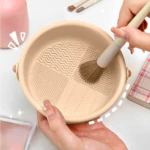 Limpiador de brochas de maquillaje beige con texturas, en uso para lavar una brocha.