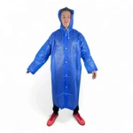 Hombre joven con capa impermeable azul brillante, con capucha, botones al frente y zapatillas rojas.