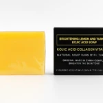 Pastilla de jabón amarillo brillante con ácido kójico y cúrcuma, empaque negro con detalles dorados.