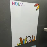 Pizarra magnética blanca con texto "NOTAS" en arcoíris y dibujos de útiles escolares.