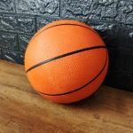 Balón de baloncesto naranja texturizado, tamaño 7, con líneas negras, sobre madera y fondo de ladrillo negro.