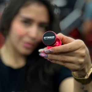 Soporte magnético rojo para celular, visto en mano con uñas decoradas, con logo STTRIKER y el texto "FEELING STRONGER".