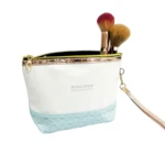 Bolso organizador de maquillaje blanco con detalle texturizado azul, cremallera dorada y brochas.