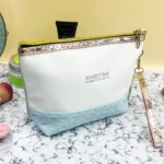 Bolso organizador de maquillaje blanco y azul con textura tejida, cremallera dorada y correa.