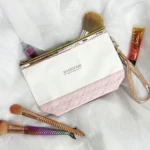 Bolso organizador de maquillaje blanco con borde rosa texturizado, cepillos y brillo labial.