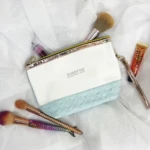 Bolso organizador de maquillaje blanco y celeste con brochas y labial.