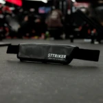 Cinturón STTRIKER para hip thrust, glúteos y pesas, en cuero sintético negro, sobre piso de gimnasio.