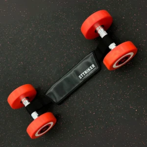 Pesas de mano con extremos rojos, conectadas por un cinturón negro de STTRIKER sobre superficie oscura con motas.