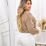Mujer con suéter cuello alto marrón y pantalón blanco ajustado, vista de espalda.