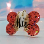 Placa de mascota hueso rojo con glitter dorado y nombre "Milo" grabado.