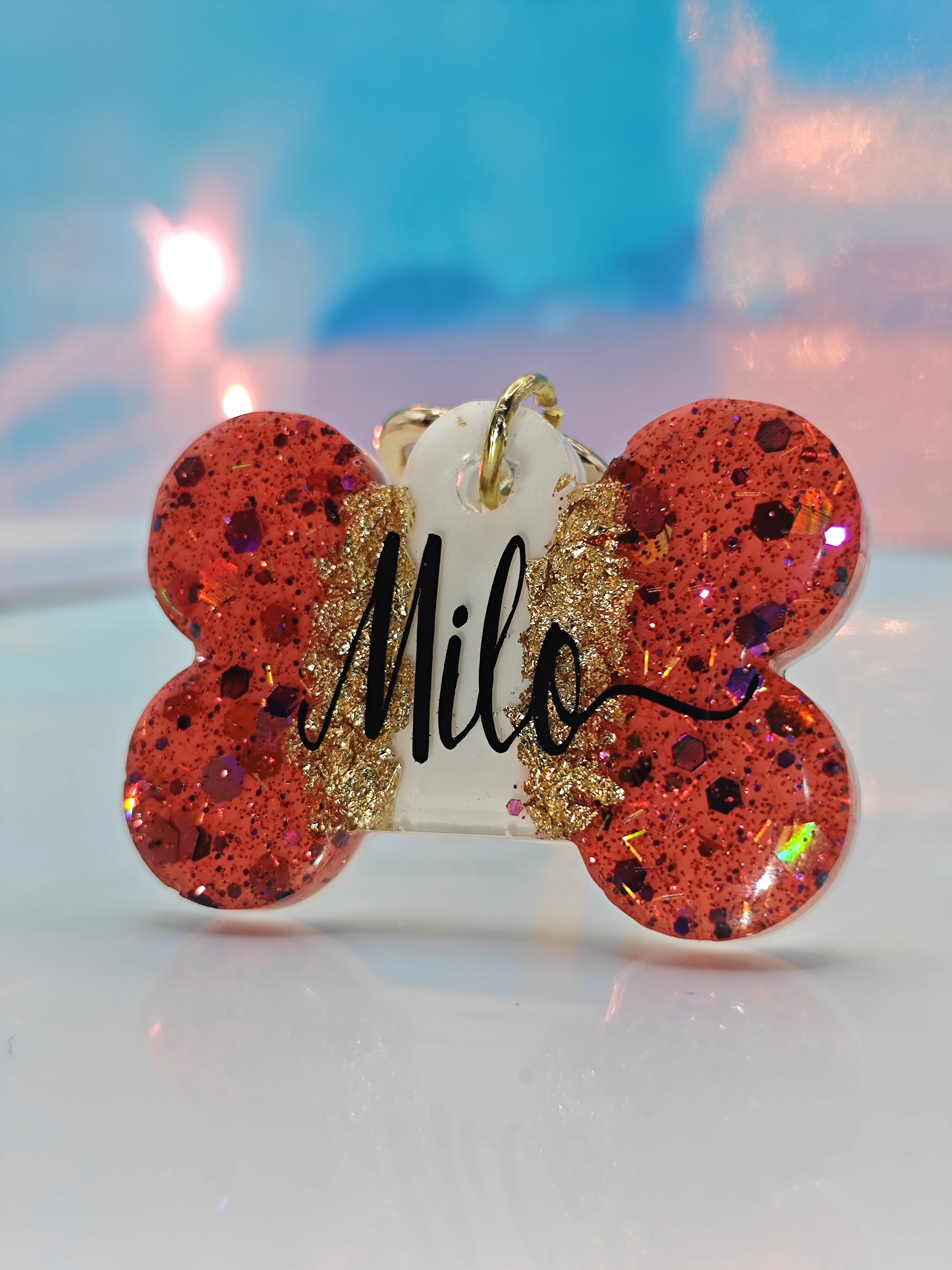 Placa de mascota hueso rojo con glitter dorado y nombre "Milo" grabado.