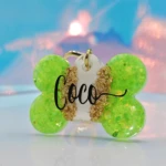 Placa hueso verde con nombre "Coco" en negro, detalles dorados, para collar de mascota.