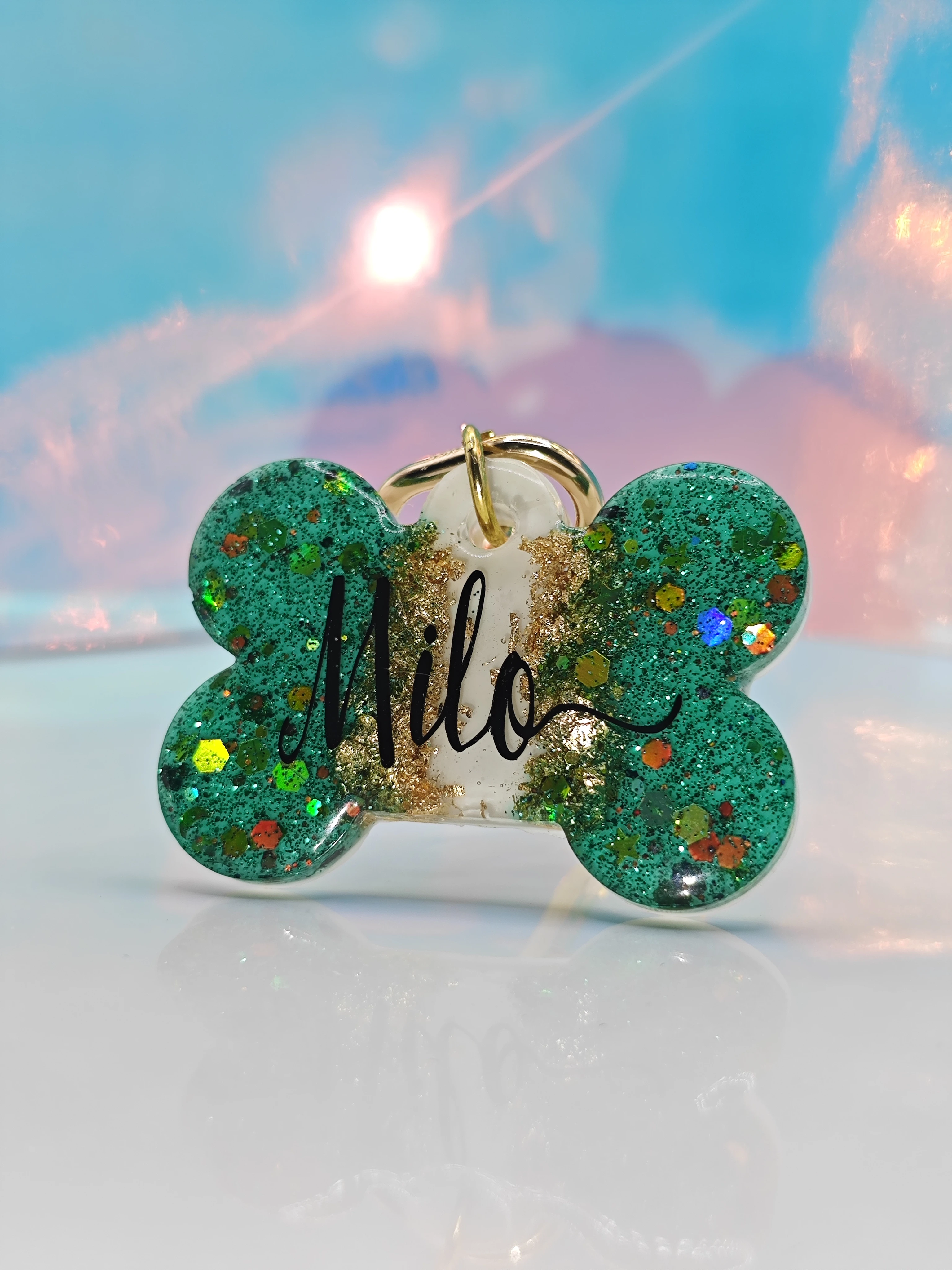 Placa de mascota de resina en forma de hueso, color verde con brillos y nombre "Milo" en negro.