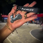 Llavero en 3D de moto NMAX gris y negro con detalle rojo, junto a un anillo y pulsera de oro en una mano.