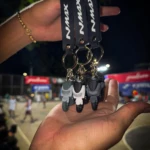 Llaveros 3D de moto NMAX grises y blancos, con correa negra, colgados en una mano.