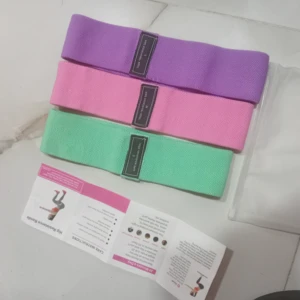 Bandas de resistencia premium para cadera: morada (L), rosa (M), verde (S). Textura de tela.