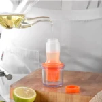 Dispensador de aceite transparente con brocha naranja, llenándose de aceite dorado.