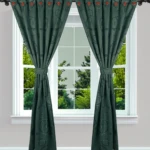 Cortina Jacquard verde oscuro con diseño de círculos, ojales rojos, atada con una banda, vista en ventana con árboles verdes.