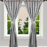 Cortinas grises con diseño jacquard y detalles rojos, atadas con pretina, sobre ventana con vista a árboles.