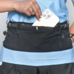 Riñonera deportiva negra con teléfono blanco siendo guardado por mano femenina.
