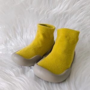 Zapatos respetuosos amarillos para bebé con suela de goma, sobre fondo blanco peludo.