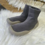 Zapatos respetuosos grises para bebé con suela de goma, textura tejida, sobre manta de pelo blanco.