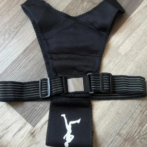 Chaleco de entrenamiento negro con soporte ajustable y figura impresa, sobre fondo de madera.