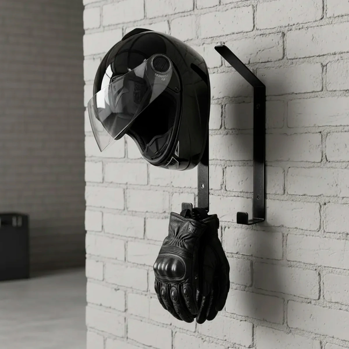 Soporte negro para casco de moto y guantes de cuero colgados en pared de ladrillos blancos.