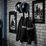 Set de dos soportes negros para cascos de moto y dos chaquetas colgando, con cuadros de motociclistas al fondo.