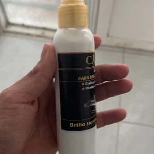 Bote spray de silicona para autos color blanco con etiqueta negra y dorada, mano sujetando el producto.