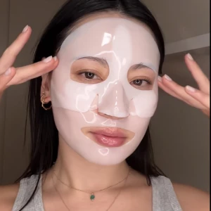 Mujer joven con mascarilla facial de biocelulosa hidratante, aplicando sobre rostro limpio.